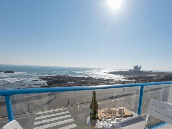 A table with a bottle and glasses, overlooking a rocky coastline and a distant castle. - Apartment Hoédic by Interhome (Quiberon)