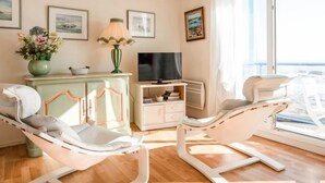 A modern living room with a reclining chair, a television, a small cabinet, and a large window with a view. - Apartment Hoédic by Interhome (Quiberon)