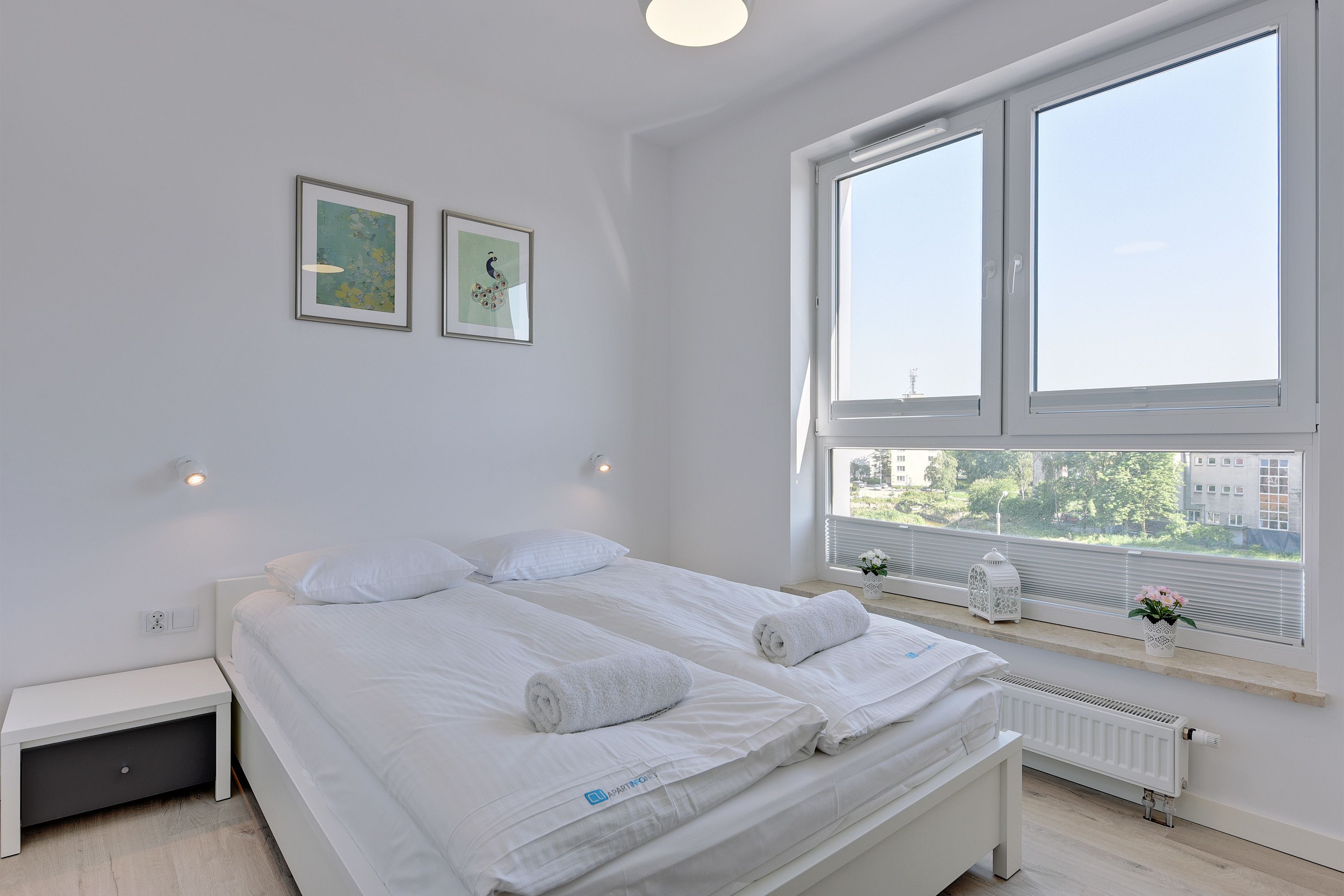 A modern bedroom with two beds, a window with blinds, and artwork on the wall.