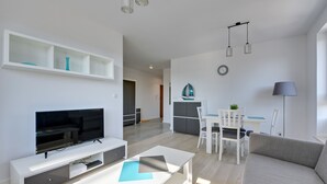 Una sala de estar moderna con televisor de pantalla plana, muebles blancos y un comedor con mesa y sillas.