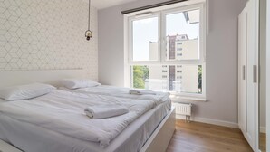 Un dormitorio moderno con una cama grande, un diseño geométrico en la pared y una ventana con vistas a edificios.