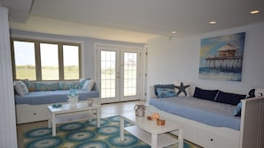 A room with a large window, a sofa, a coffee table, and a painting of a pier.