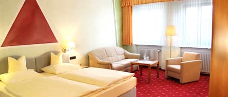A hotel room with a bed, two armchairs, a small table, and a lamp.