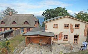 A house with a thatched roof and a brick facade, a covered patio with outdoor furniture, and a view of the water. - 05 Holiday apartment Leberblümchen - Haus am Höft in Gager with lake view and sauna (Gager)