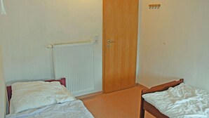 A room with two single beds, a wooden door, a radiator, and a wall-mounted light fixture. - 05 Holiday apartment Leberblümchen - Haus am Höft in Gager with lake view and sauna (Gager)