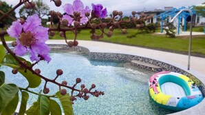 A swimming pool with a colorful inflatable ring, surrounded by blooming flowers and a blue structure in the background. - Kenting Bay Homestay III (Hengchun)