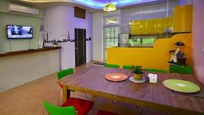 A modern dining area with a wooden table, green and red chairs, a potted plant, and a television on the wall. - Kenting Bay Homestay III (Hengchun)