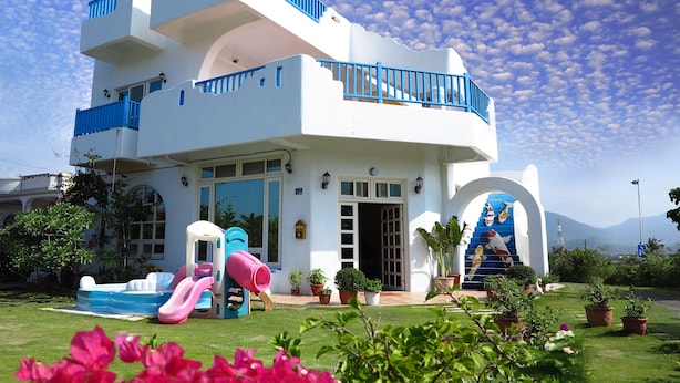 A two-story building with a white exterior and blue accents, featuring a children's play area with a slide and inflatable pool, surrounded by potted plants and a clear sky. - Kenting Bay Homestay III (Hengchun)