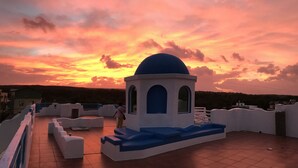 A rooftop terrace with a white and blue structure, a tiled floor, and a view of the sunset. - Kenting Bay Homestay III (Hengchun)