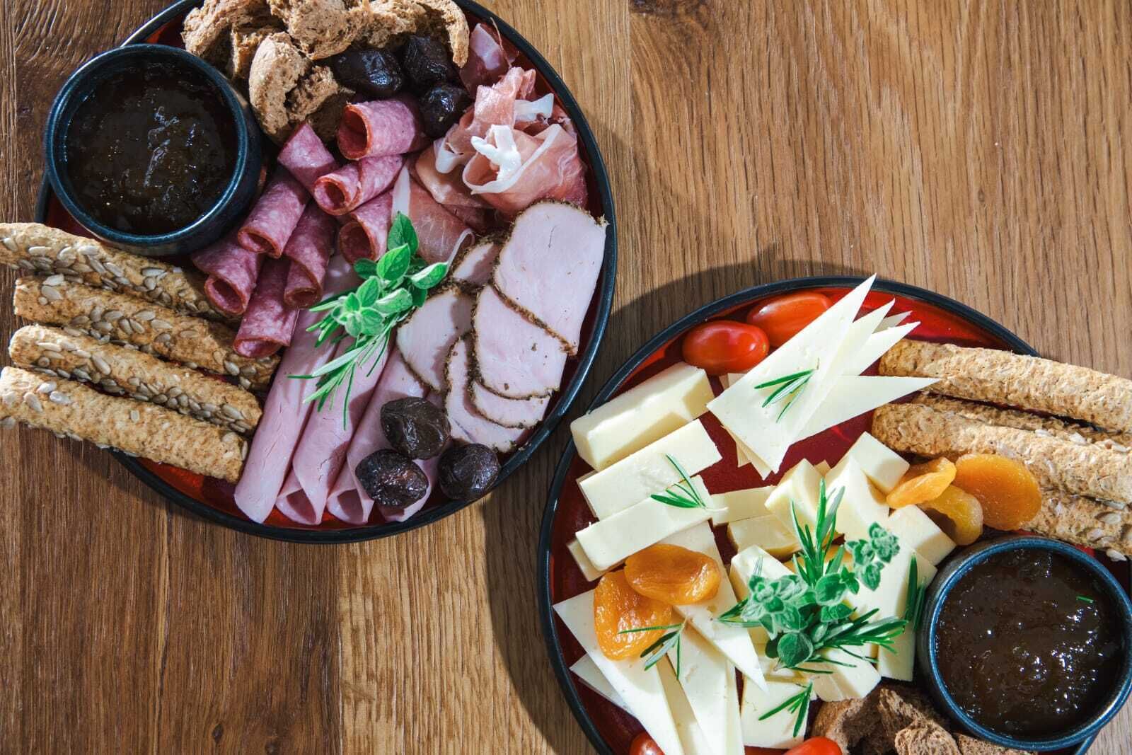 Two charcuterie boards with various meats, cheeses, and crackers.