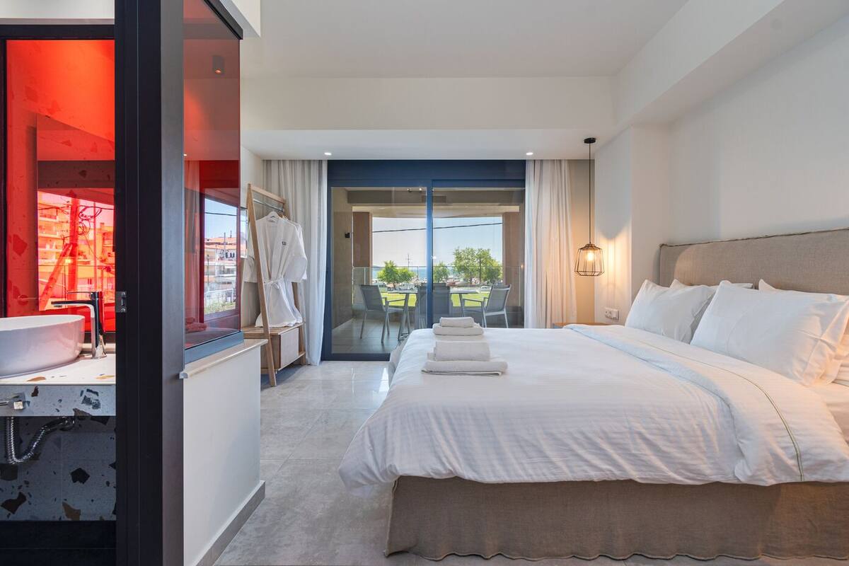 A modern hotel room with a large bed, a bathroom with a sink, and a balcony with a view.