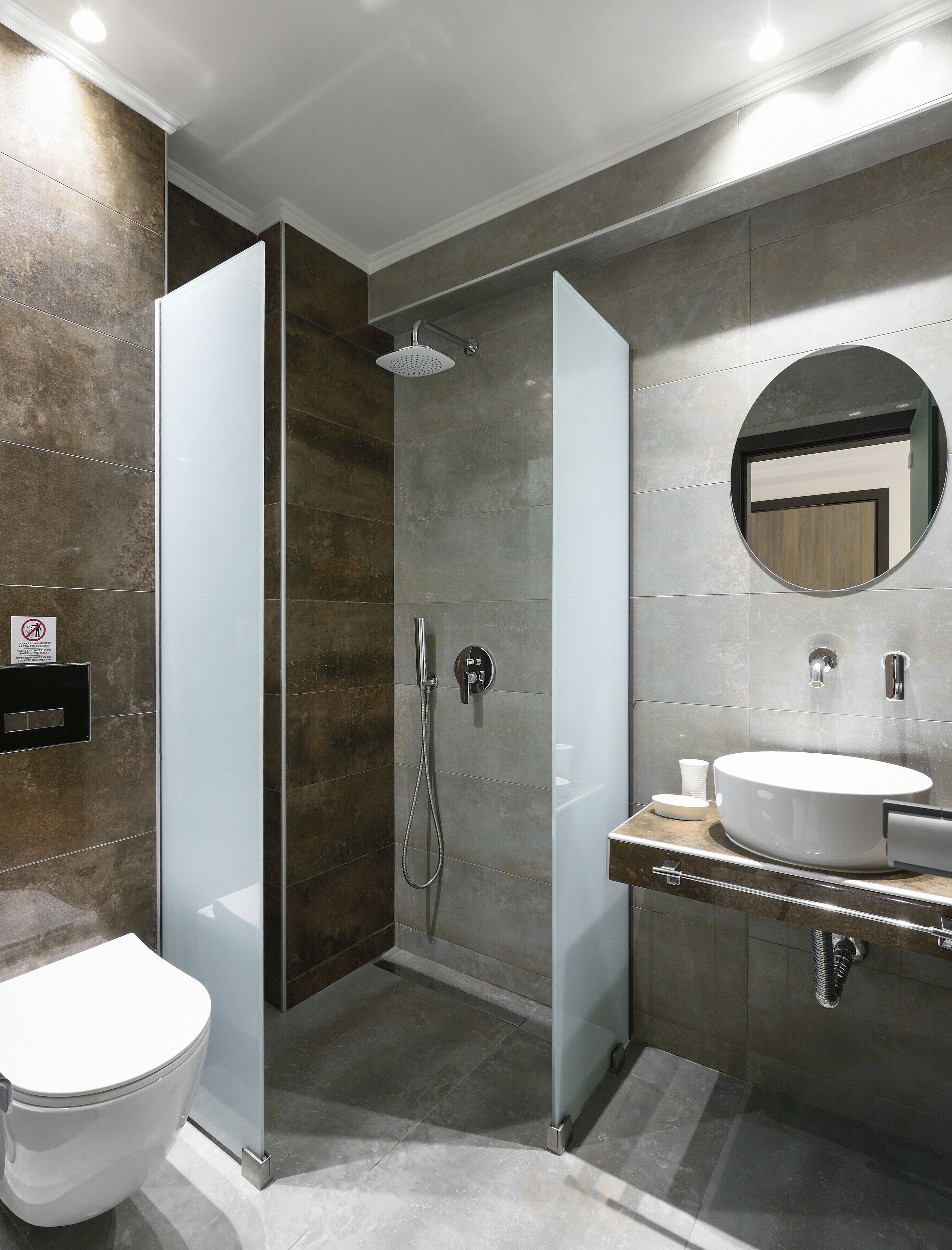 A modern bathroom with a glass-enclosed shower, a round mirror, and a white sink.