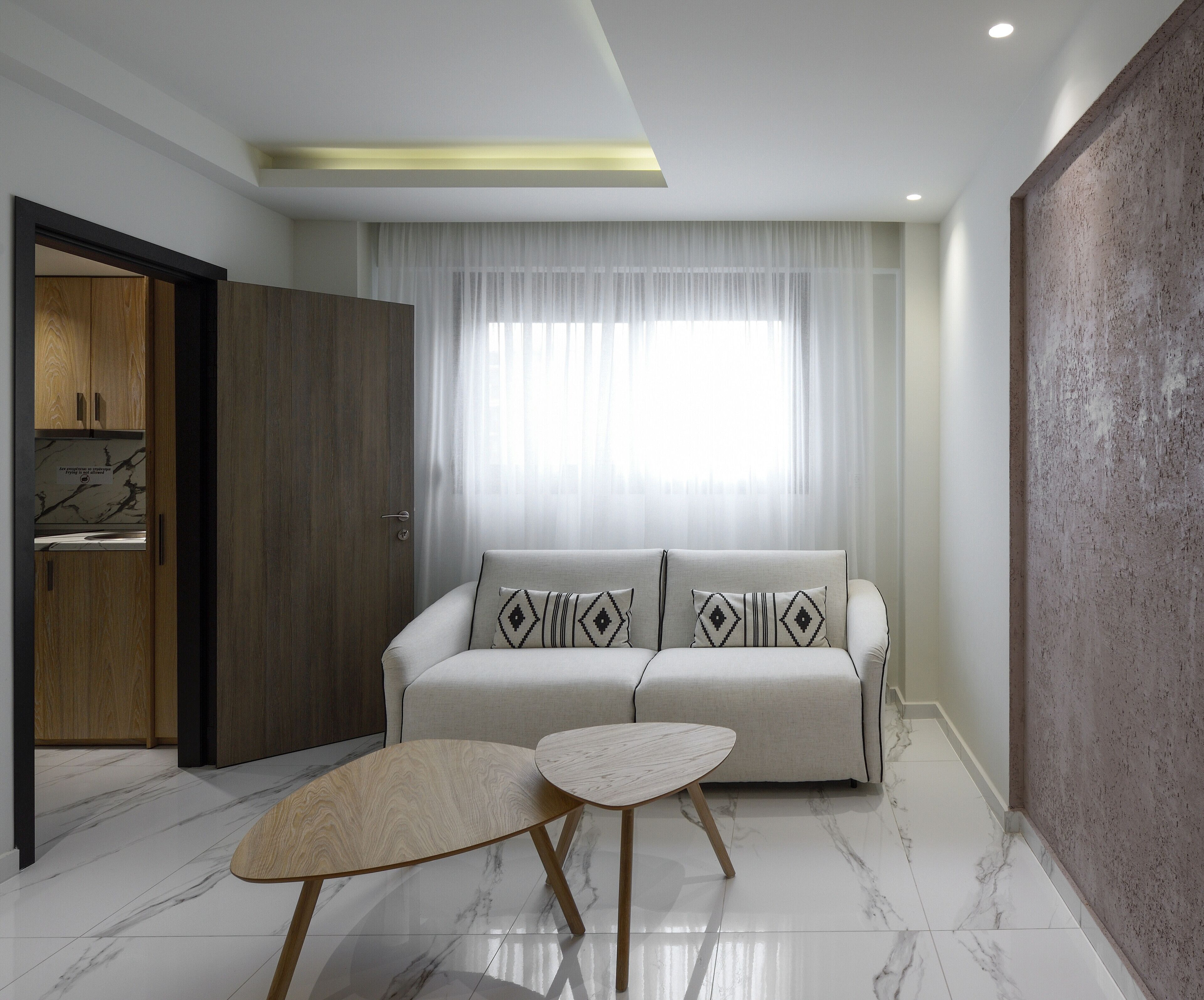 Una sala moderna con un sofá, dos mesas auxiliares y un ventanal con cortinas traslúcidas.