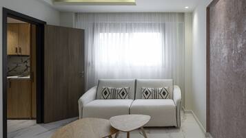 Una sala moderna con un sofá, dos mesas auxiliares y un ventanal con cortinas traslúcidas.