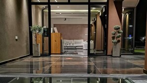 En moderne hotellobby med en receptionsdisk i marmor, et siddeområde med sofa og lænestole, samt en glasvæg.