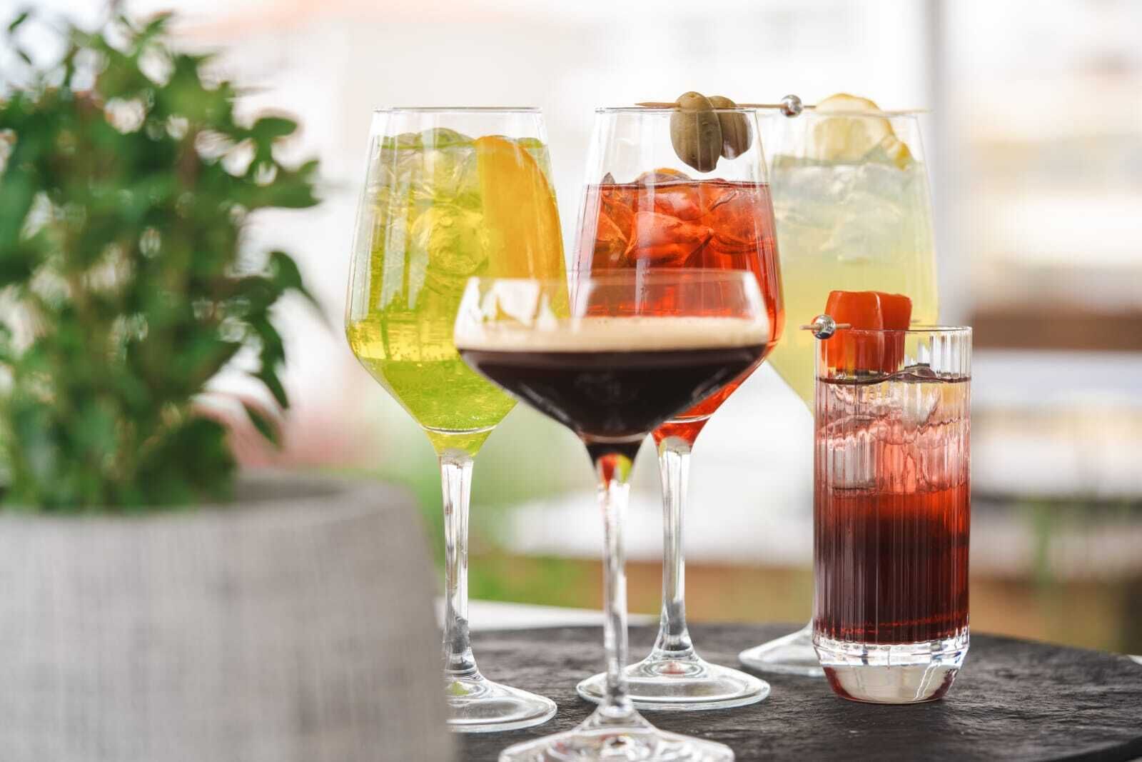 Quatro cocktails diferentes em copos diversos sobre uma mesa.