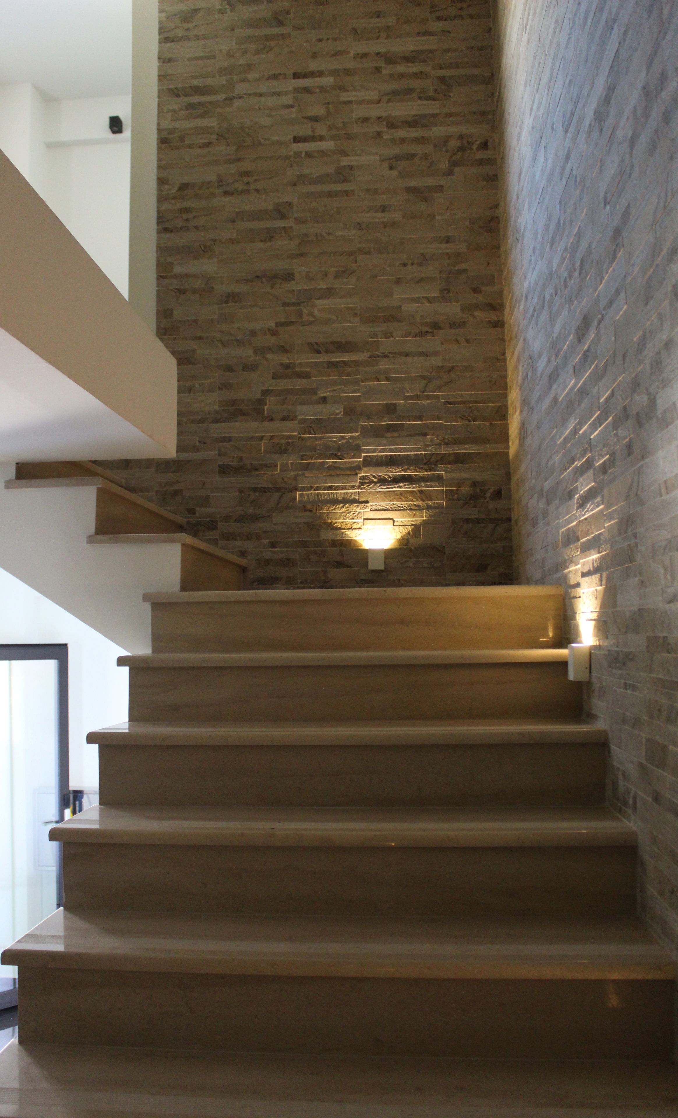 A staircase with a stone wall on one side and a white wall on the other, leading to a higher floor.