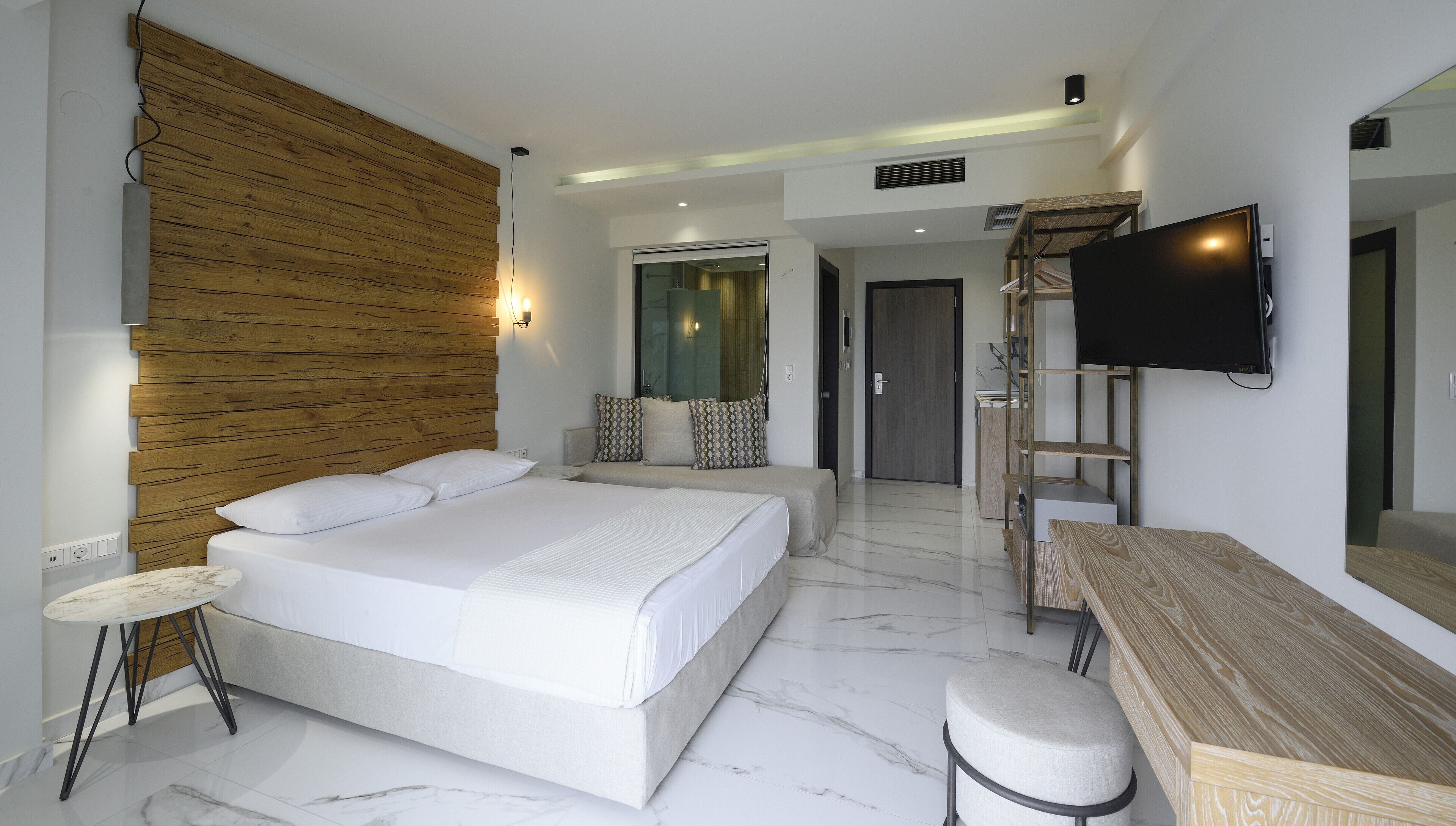 A modern hotel room with a large bed, a desk, a chair, and a TV mounted on the wall.