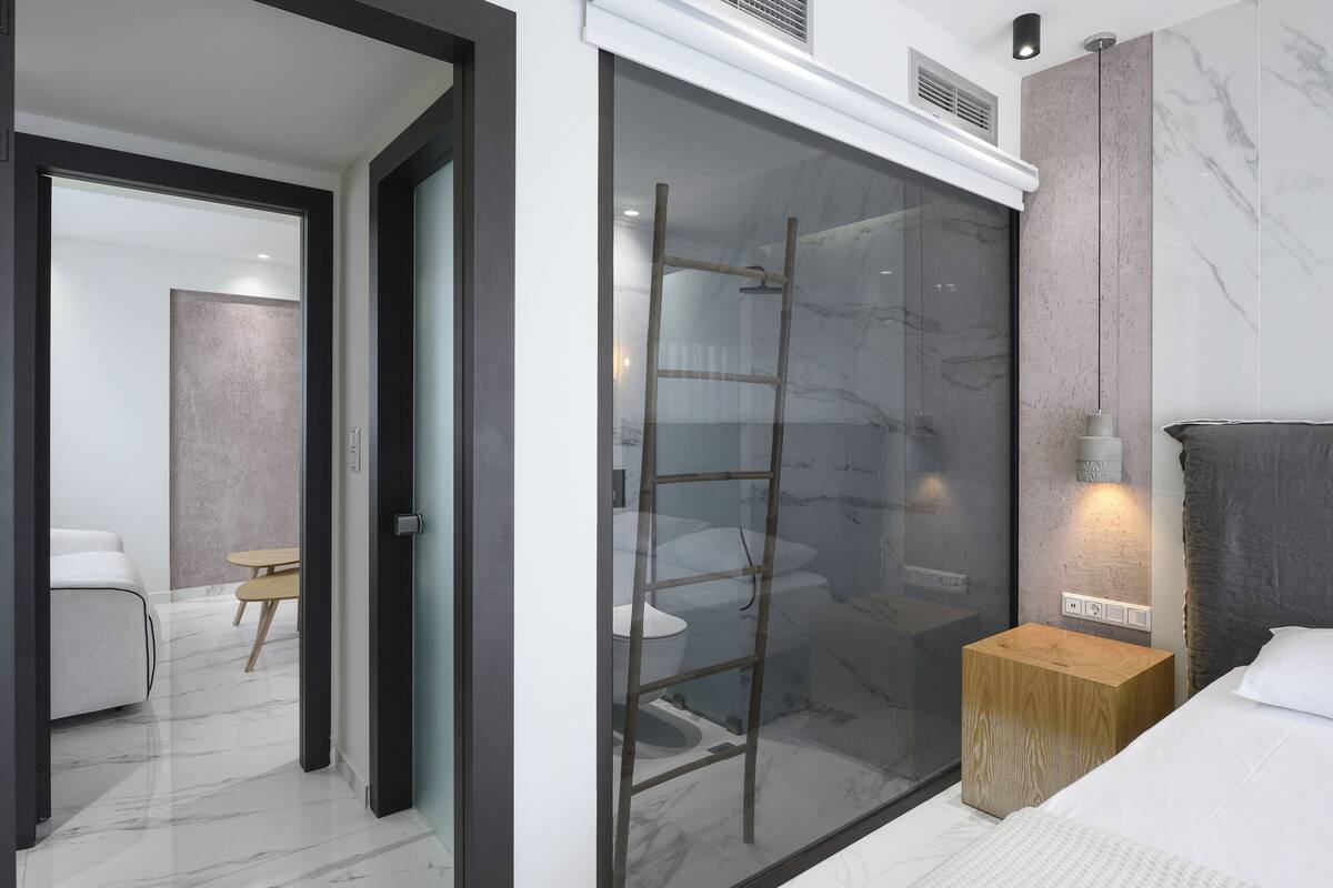 A modern bedroom with a glass shower enclosure, a wooden bedside table, and a white bed.