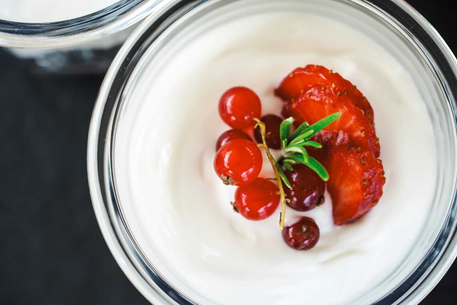 A close-up of a dessert with strawberries and red currants on a creamy base.