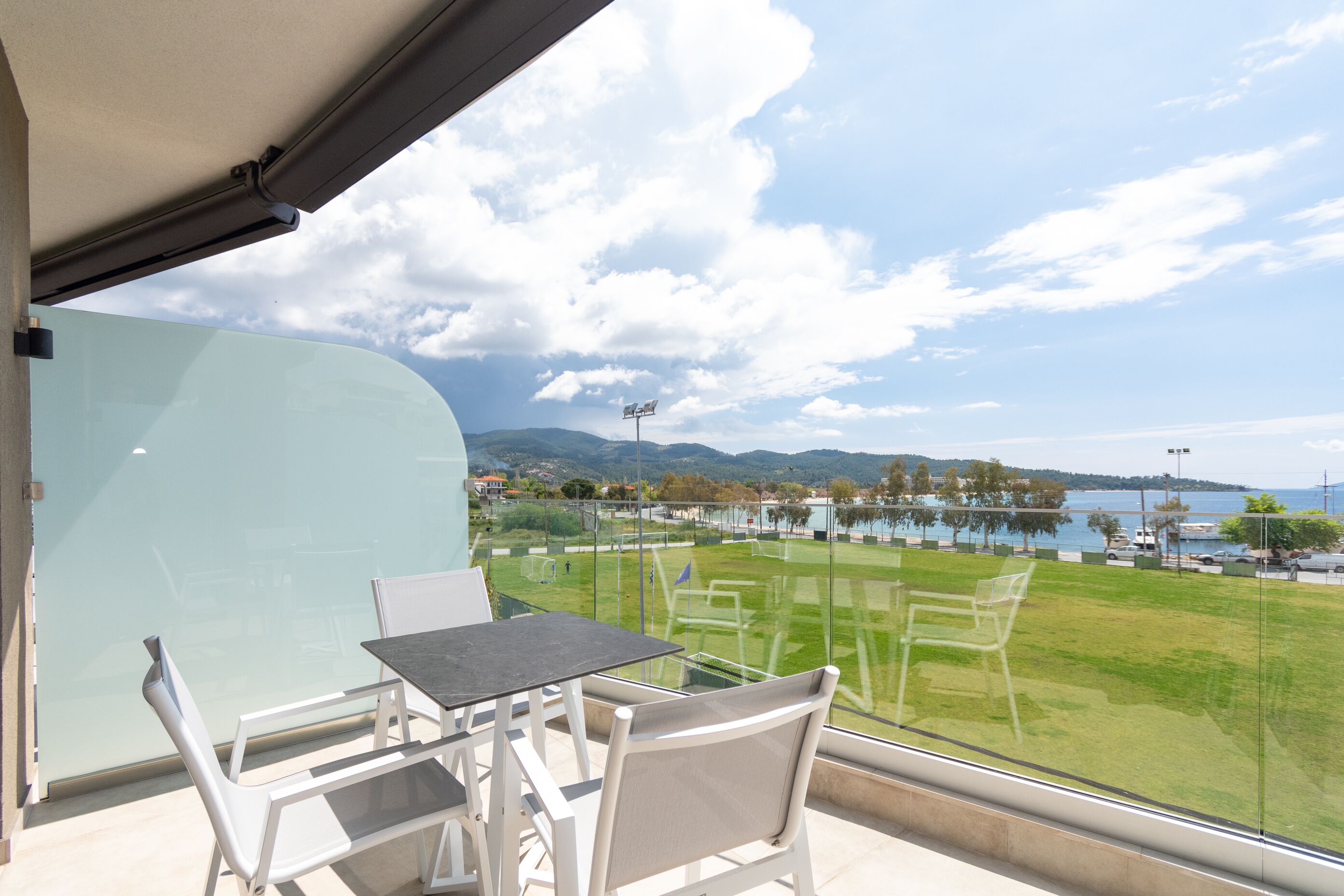 A balcony with a table and chairs, overlooking a grassy area and a body of water.