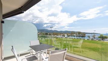 A balcony with a table and chairs, overlooking a grassy area and a body of water.