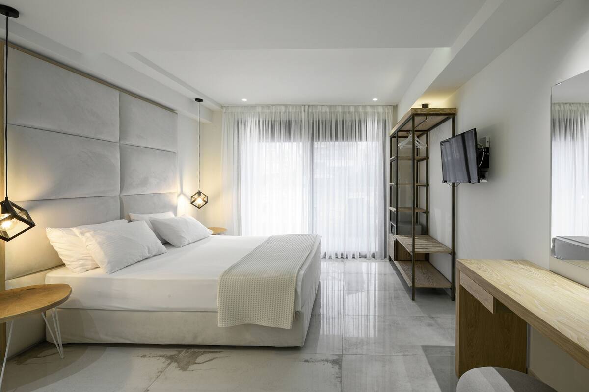 A modern bedroom with a large bed, a bedside table, a mirror, and a TV mounted on the wall.