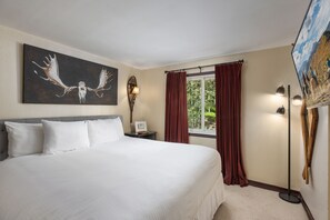A hotel room with a large bed, a painting of antlers, a window with curtains, a lamp, and a wall-mounted picture. - Terracehouse 93 - Steps to Slopes | Inviting Mountain Retreat, Pool & Hot Tub (Snowmass Village)