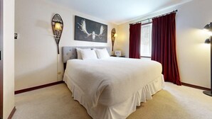 A bedroom with a large bed, two wall-mounted lamps, a window with red curtains, and a painting on the wall. - Terracehouse 93 - Steps to Slopes | Inviting Mountain Retreat, Pool & Hot Tub (Snowmass Village)