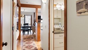 Een hal met een houten plafond, een eetgedeelte met een tafel en stoelen, en een keuken met kasten en een fornuis.