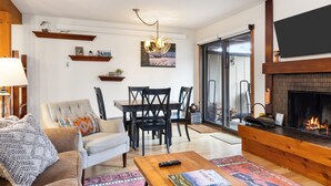 Een woonkamer met een open haard, een bank, een salontafel en een eethoek met stoelen en een tafel.