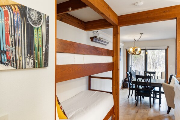 A bunk bed with a wooden headboard, a dining area with a table and chairs, and a wall-mounted ski rack.
