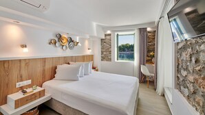 Une chambre d’hôtel moderne dotée d’un grand lit, d’une télévision, d’un mur décoratif en pierre et offrant une vue sur la mer.