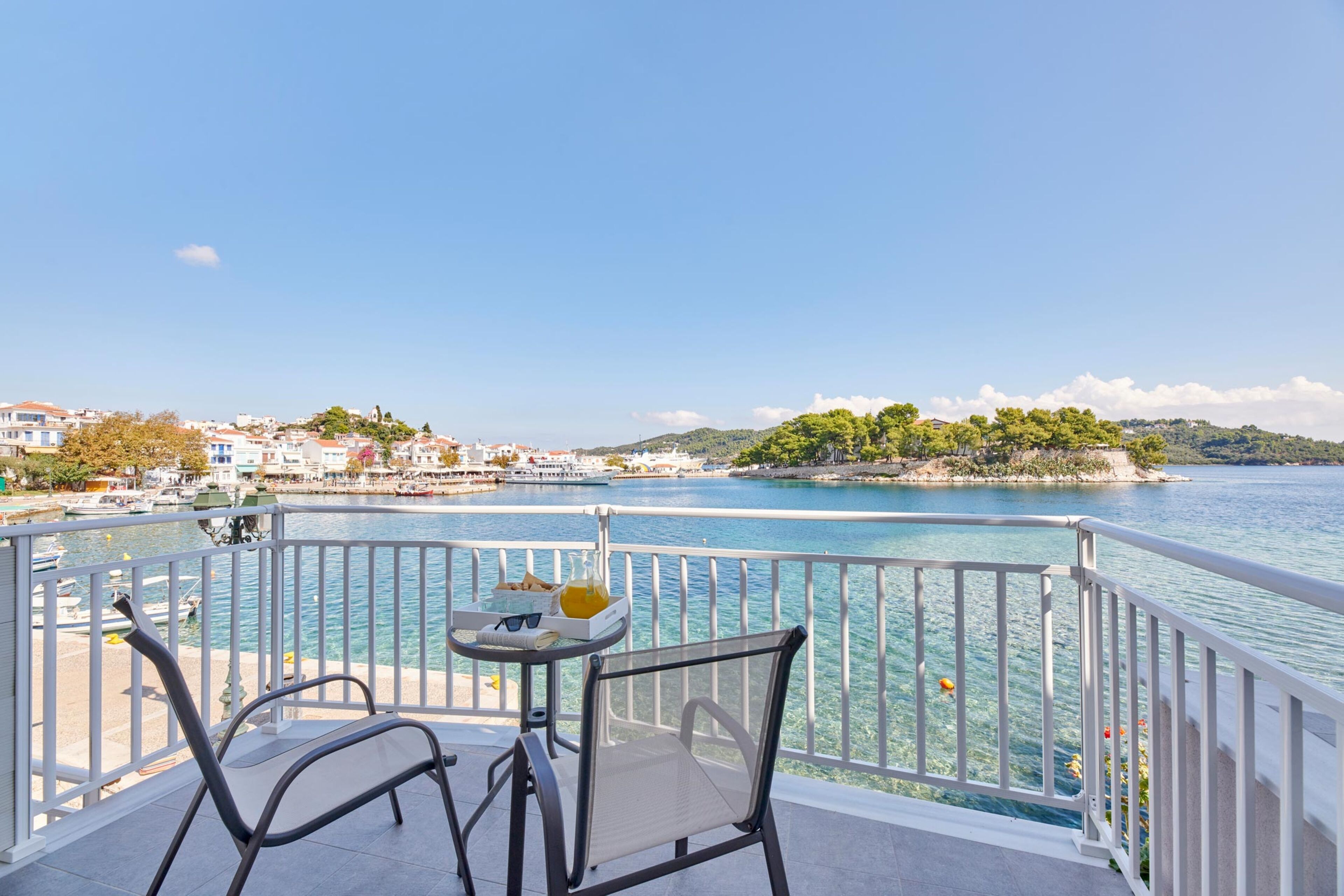A balcony with a table and chairs overlooking a body of water with a view of the coastline and buildings.