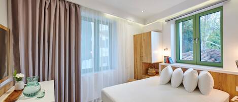 Quarto de hotel moderno com uma cama grande, mesa de cabeceira, cômoda e uma janela com cortinas.