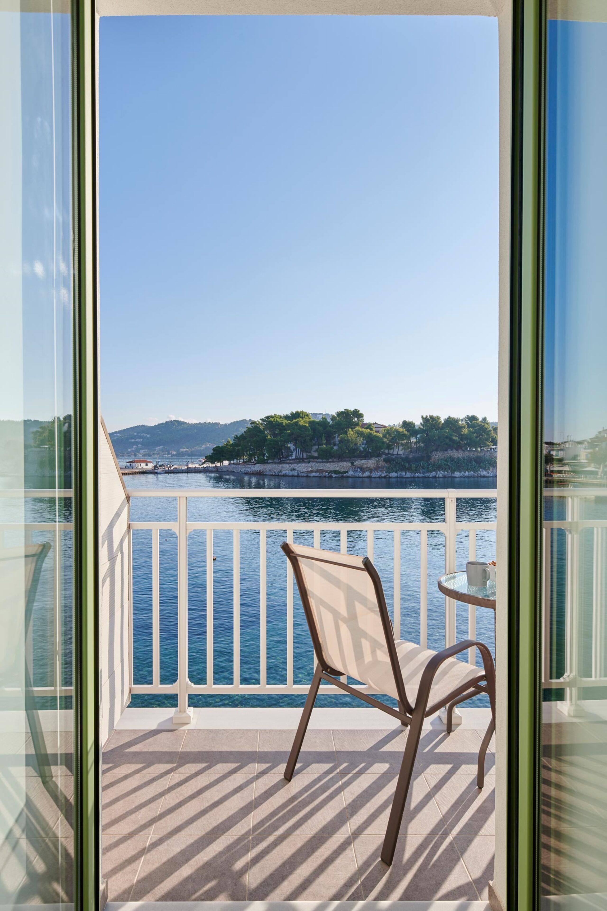 Un balcón con una silla y una mesa, con vista a un cuerpo de agua y una orilla lejana.