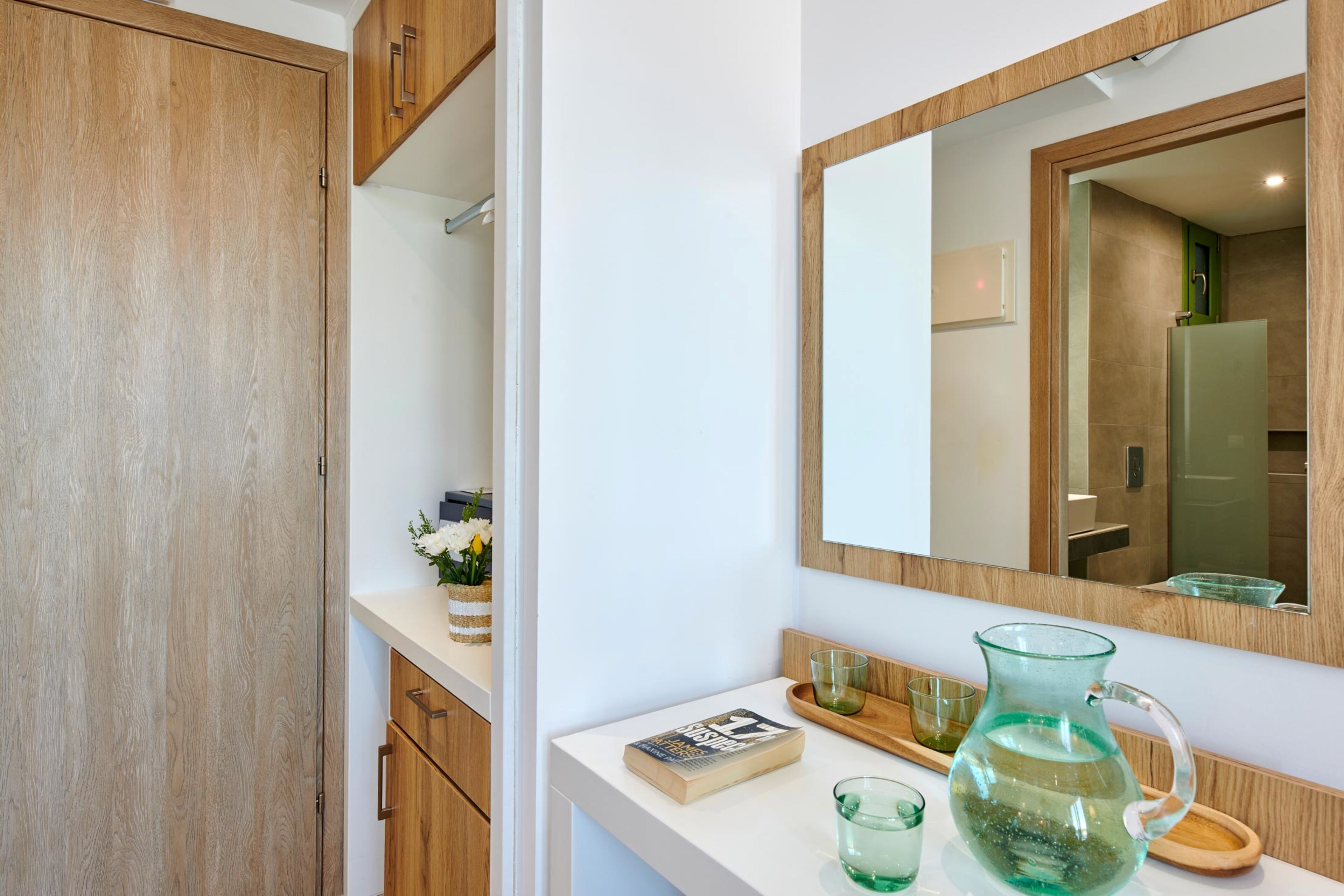 A bathroom with a wooden vanity, a mirror, a book, and a glass pitcher.