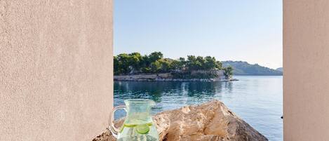 A table with a pitcher and two glasses of water, overlooking a body of water and a tree-lined island.
