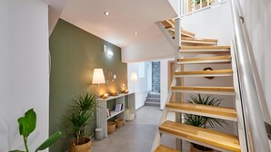 Un intérieur moderne avec un escalier, des étagères remplies de livres et d’objets décoratifs, et des plantes en pot.