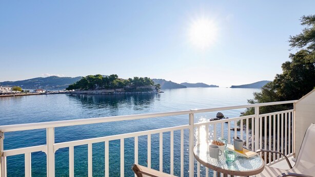 Un balcon offrant une vue dégagée sur une mer calme, une île lointaine et un paysage montagneux en arrière-plan.