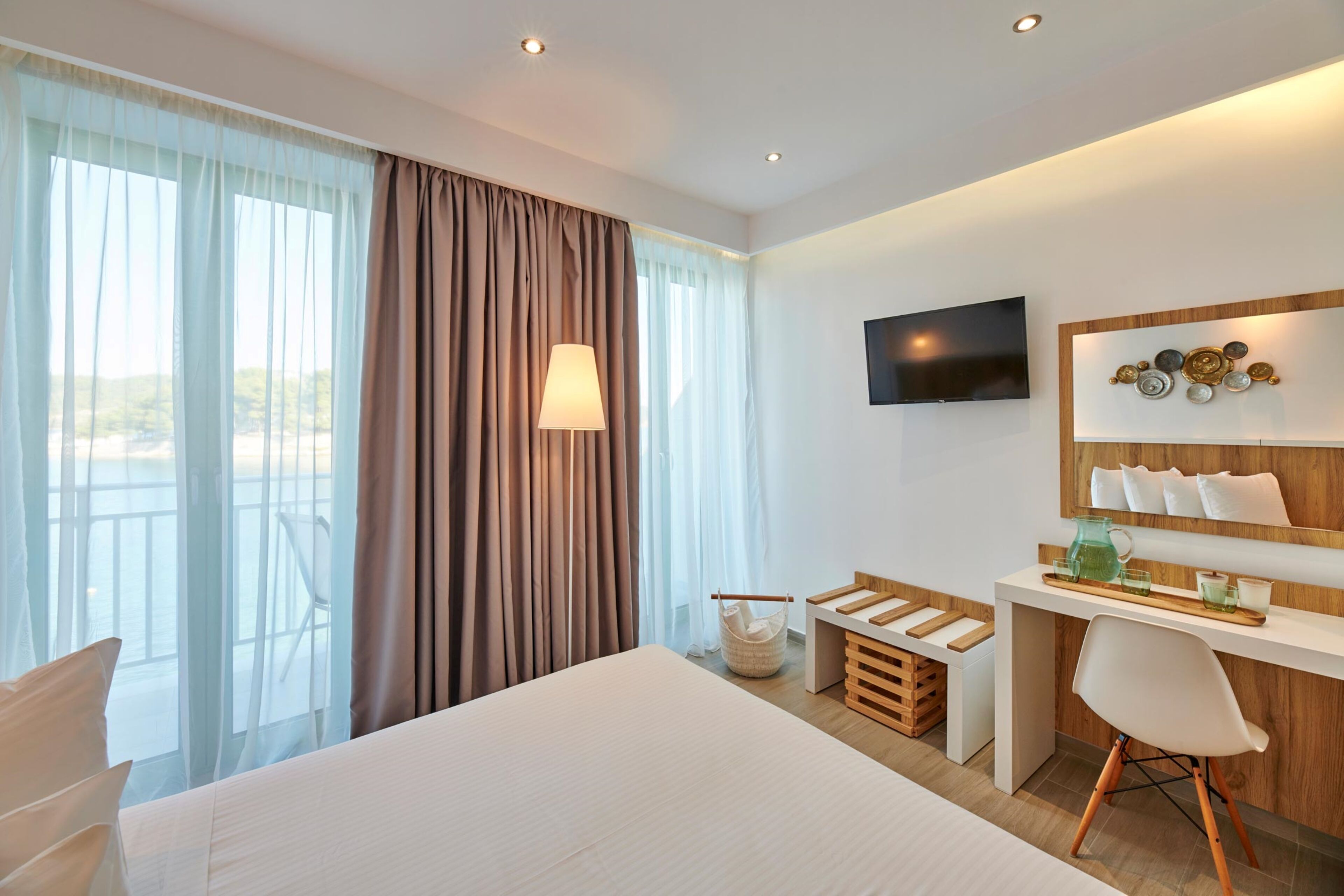 A hotel room with a bed, a desk, a chair, a television, and a view of the outdoors.