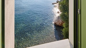 Une vue à travers une fenêtre sur une étendue d’eau aux eaux claires, une côte rocheuse et des reliefs lointains.