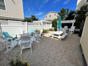 En patio med Adirondack-stole, et picnicbord og en pergola med en grøn parasol.