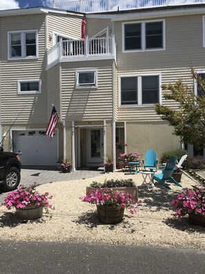 Stroll up to the charming front entrance, where a balcony and porch await, surrounded by lush greenery and a welcoming outdoor seating area.