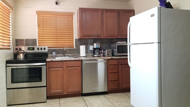 A kitchen with wooden cabinets, a stainless steel refrigerator, a microwave, a toaster, a coffee maker, and a dishwasher. - A Gem in the Heart of Tucson (Tucson)