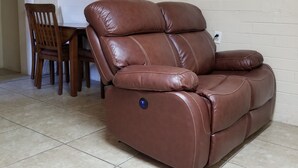 A brown leather reclining sofa with a power button, positioned in a room with a tiled floor and a white brick wall. - A Gem in the Heart of Tucson (Tucson)