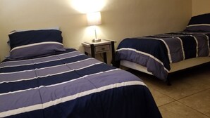A room with two beds, each with striped bedding, a bedside table, and a wall-mounted lamp. - A Gem in the Heart of Tucson (Tucson)