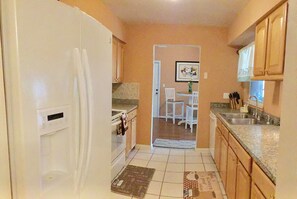 A compact kitchen with white cabinets, a refrigerator, a dining area with a table and chairs, and a tiled floor. - Nice and quite vacation home (Tampa)
