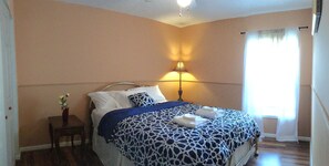 A neatly made bed with a patterned bedspread, a bedside table with a vase of flowers, and a lamp providing soft lighting. - Nice and quite vacation home (Tampa)