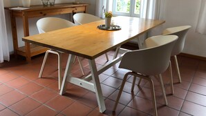 A dining area with a wooden table and four white chairs. There is a small table with a lamp and a vase with flowers. A window with curtains is visible in the background. - Vacation home 2 - Holiday homes Michaelis 1 to 4 in Quilitz (Rankwitz)